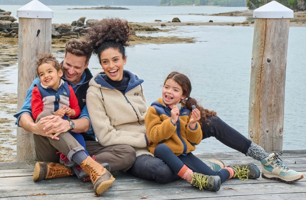 A family of four wearing warm clothes and sitting on an old wooden doc